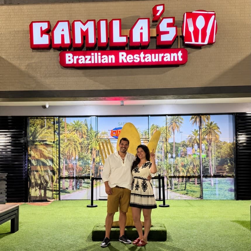 Casal na entrada do Camila's, com o garfo dourado atrás