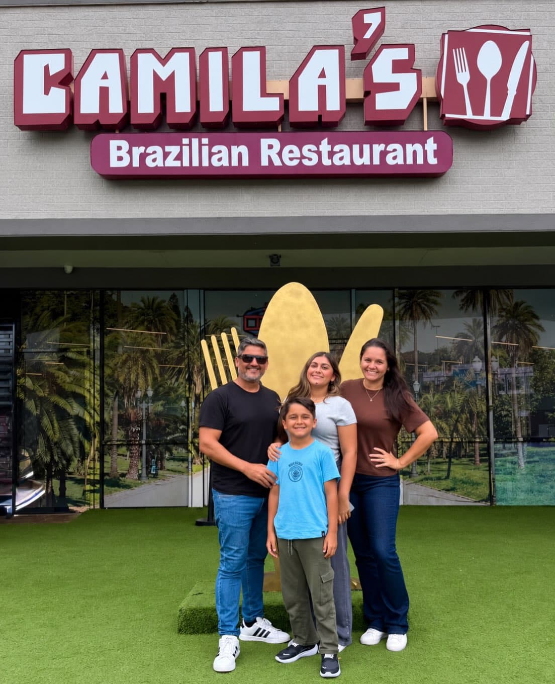 Família de quatro na frente do garfo e da colher gigantes