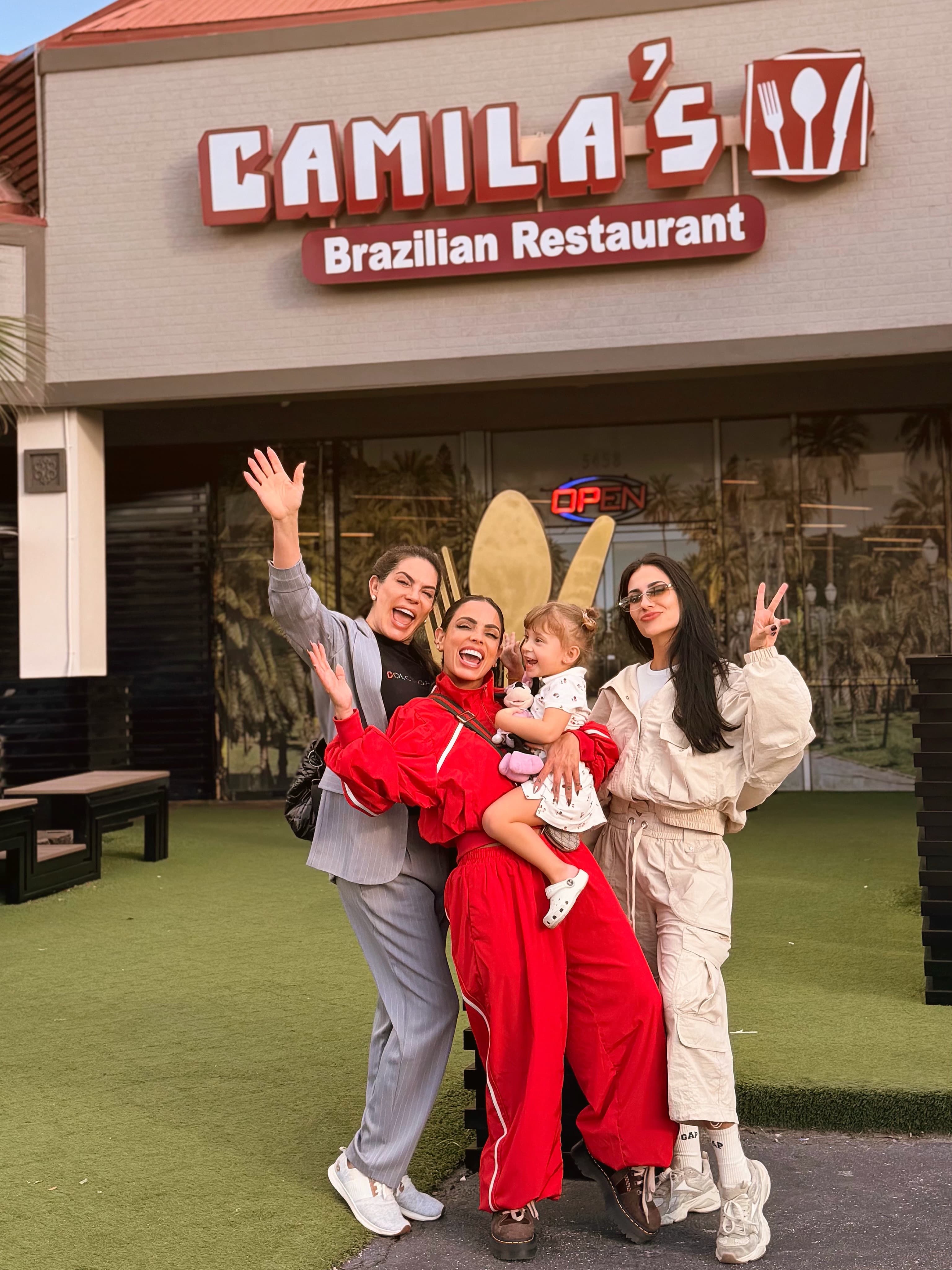 Família com criança no colo acenando na frente do restaurante